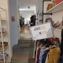 Winkelinterieur met prijsbord 'JEDES TEIL 1€ - 2€' en rekken met tweedehands kleding