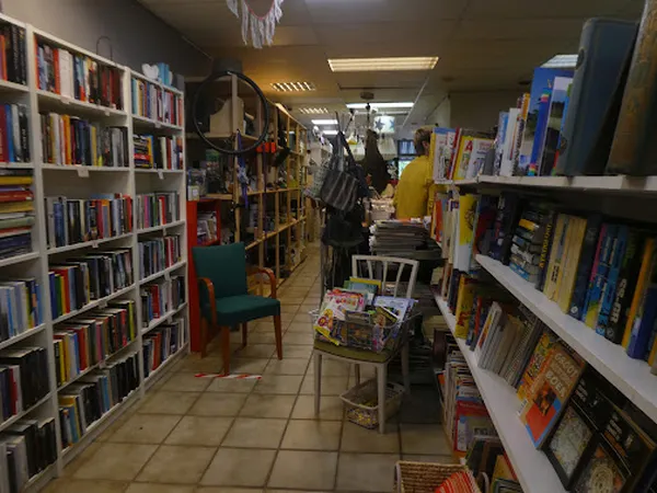 Winkelinterieur met boekenrekken aan beide zijden, stellingen met articles in het midden, en een groene stoel.