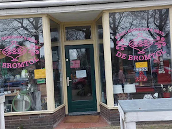 Winkelpui met twee grote ramen met roze logo's en groene deur, bakstenen onderkant, winkelnaam zichtbaar op ramen