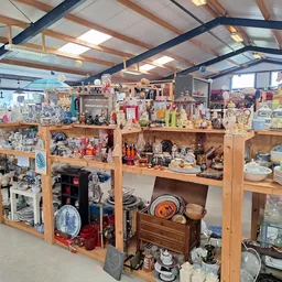 Houten stellingen met serviesgoed, huishoudartikelen en diverse spullen in een kringloopwinkel