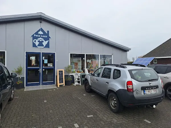 Grijze gevel van kringloopwinkel met blauwe deuren en Poco Loco-logo, parkeerplaats met auto's ervoor