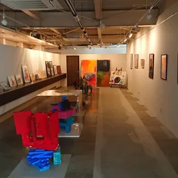 Kunstgalerij-achtig interieur met rode en blauwe sculpturen, schilderijen aan de wanden en geïndustrialiseerd plafond