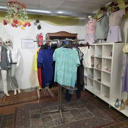 Winkelinterieur met kledingrekken, mannequins in outfits, witte stellingen met spullen, bloemenslinger decoratie en diverse k