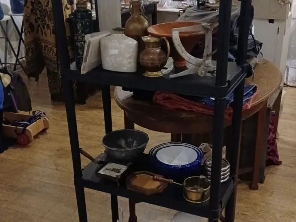 Zwarte metalen stellage met keramische schalen, pannen, kannen en ander huishoudelijk servies