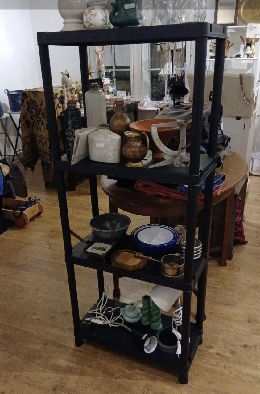 Zwarte metalen stellage met keramische schalen, pannen, kannen en ander huishoudelijk servies
