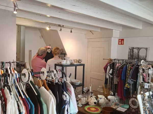 Kringloopwinkel interieur met kledingrekken, toonbank en twee bezoekers die rondkijken