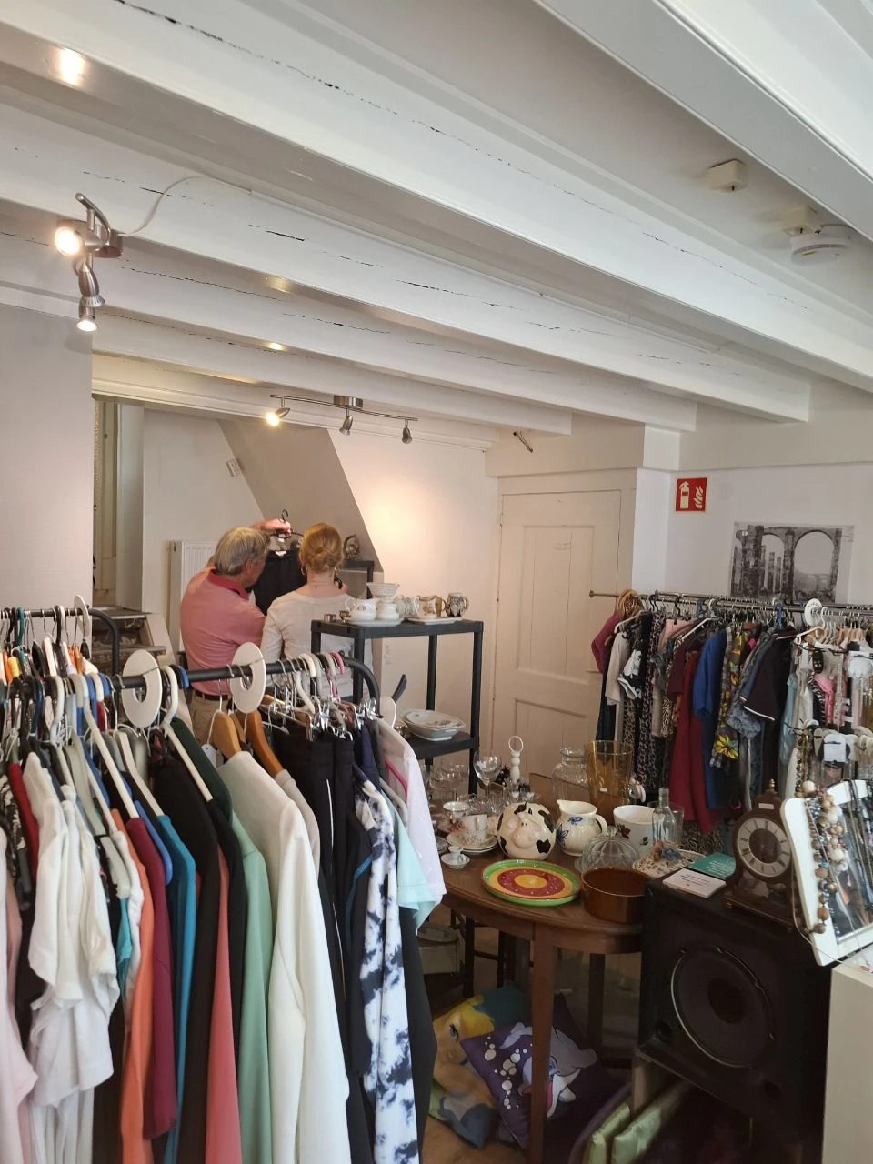 Kringloopwinkel interieur met kledingrekken, toonbank en twee bezoekers die rondkijken