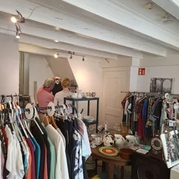 Kringloopwinkel interieur met kledingrekken, toonbank en twee bezoekers die rondkijken