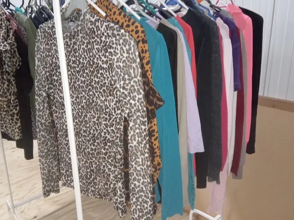 Rekken met tweedehands dameskleding in verschillende kleuren en patronen, waaronder luipaardprint en effen kleuren