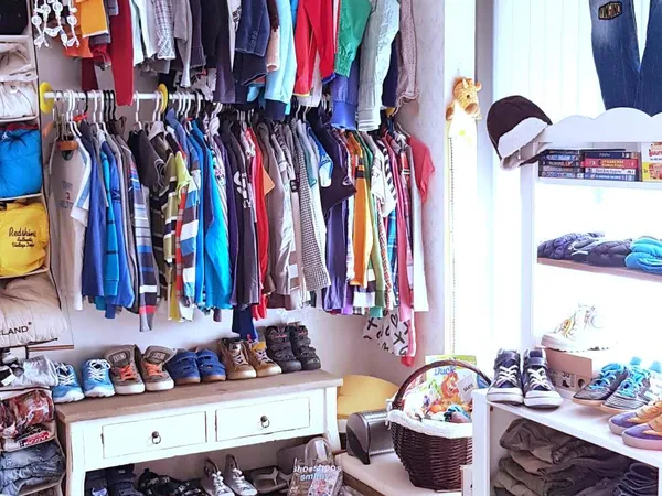 Winkelbinnenruimte met kledingrekken aan muur, stellingen met schoenen en accessoires, en opbergmanden op de grond