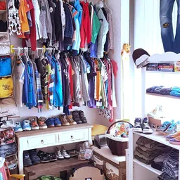 Winkelbinnenruimte met kledingrekken aan muur, stellingen met schoenen en accessoires, en opbergmanden op de grond
