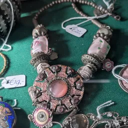 Zilverkleurige sieraden met roze stenen en parels op groen display, inclusief hangers en kralen