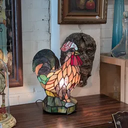 Tiffany-stijl glazen lamp in de vorm van een haan met gekleurde glaswerk, naast een bronzen buste