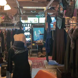 Winkelinterieur met kledingrekken, hangende kleding, rode loper en blauwe deur naar achterkamer