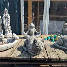 Stenen beelden en tuinkatten op houten terras buiten de winkel