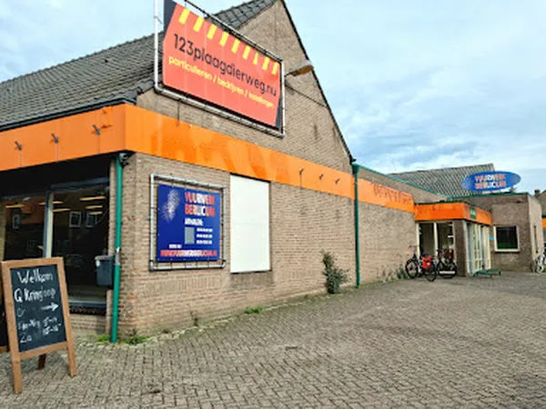 Voorgevel van kringloopwinkel met oranje luifel, blauwe informatiebord en winkelingang