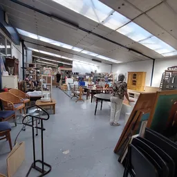 Ruim interieur van kringloopwinkel met diverse meubels, stoelen en huishoudelijke spullen uitgestald
