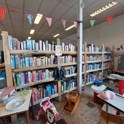Binnenkant van kringloopwinkel met boekenkasten, speelgoed en kinderafdeling met gekleurde vlaggetjes als versiering