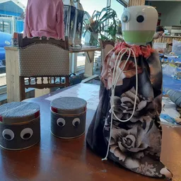 Drie zelfgemaakte figuren van kringloopmateriaal: twee cilindervormige vormen met ogen en een staande figuur met kleding op t