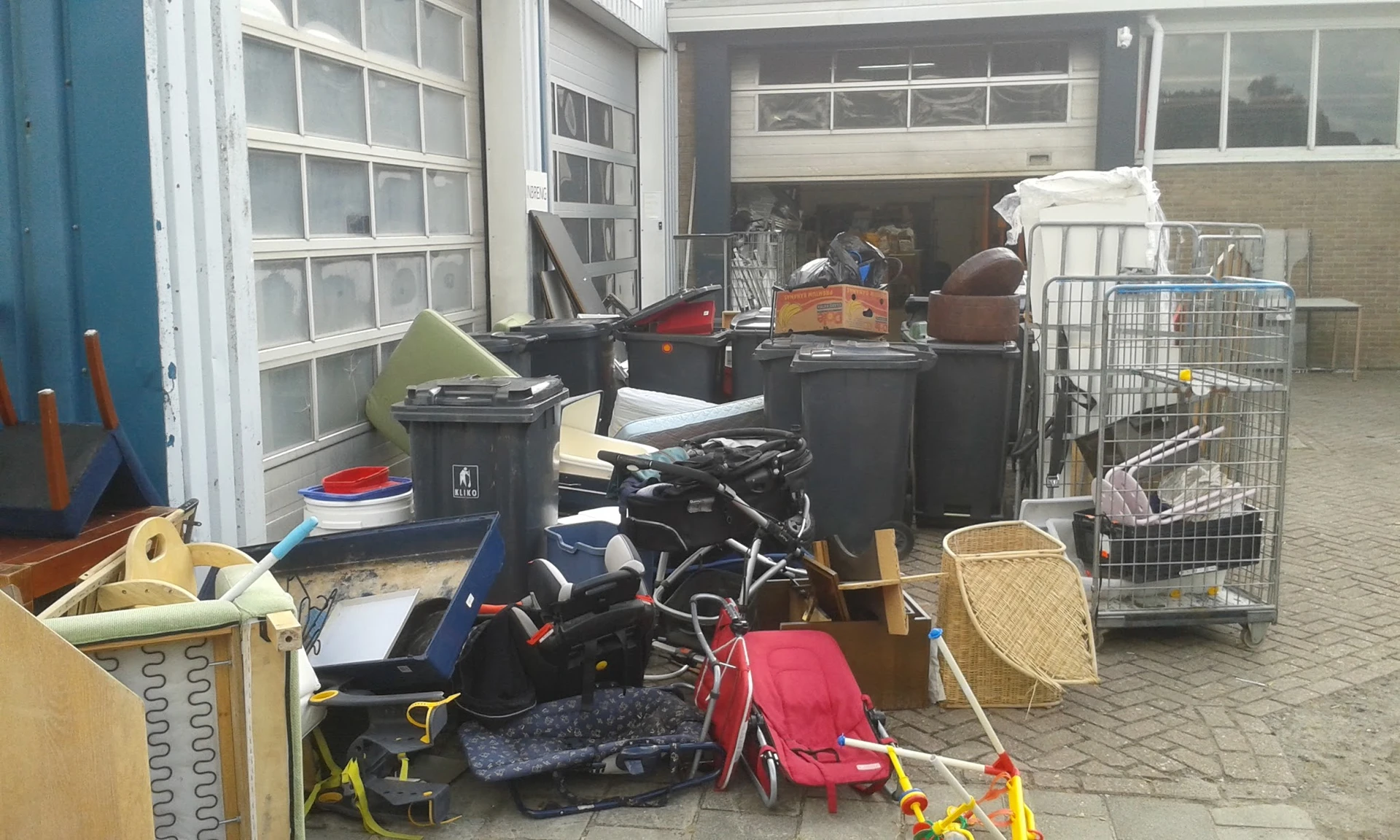 Diverse tweedehands spullen in een garage: scooter, fiets, manden, dozen en huishoudartikelen