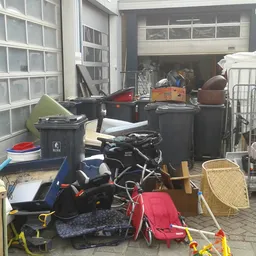 Diverse tweedehands spullen in een garage: scooter, fiets, manden, dozen en huishoudartikelen