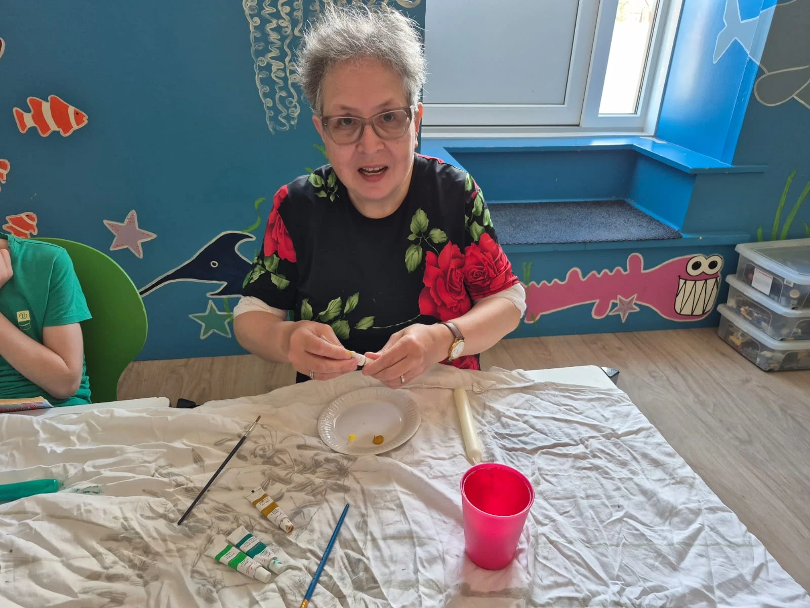 Vrijwilliger of medewerker voert kinderknutselactiviteit uit aan tafel met kunst- en knutselmaterialen