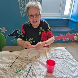 Vrijwilliger of medewerker voert kinderknutselactiviteit uit aan tafel met kunst- en knutselmaterialen