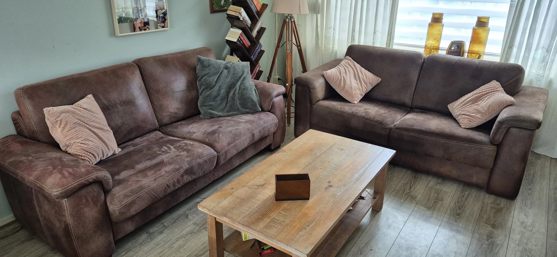 Woonkamer met twee bruine zitbanken, houten salontafel en diverse meubels en decoratie
