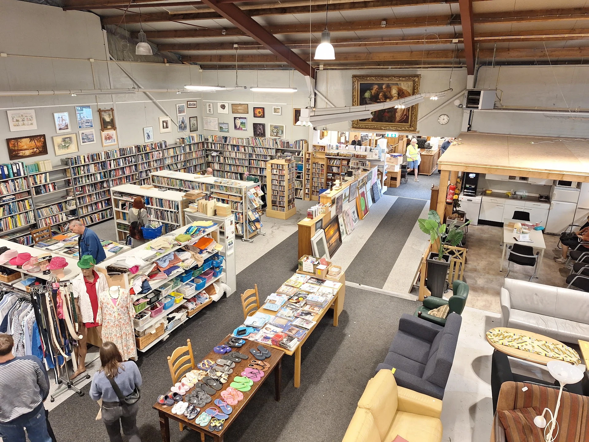 Overzicht van kringloopwinkel met boekenkasten, tafels met boeken en dvd's, kleding, meubels en decoratieartikelen