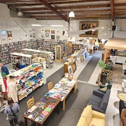 Overzicht van kringloopwinkel met boekenkasten, tafels met boeken en dvd's, kleding, meubels en decoratieartikelen