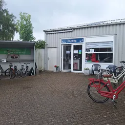 Voorkant van kringloopwinkel met ingang, ramen en uitgestalde fietsen op het terras