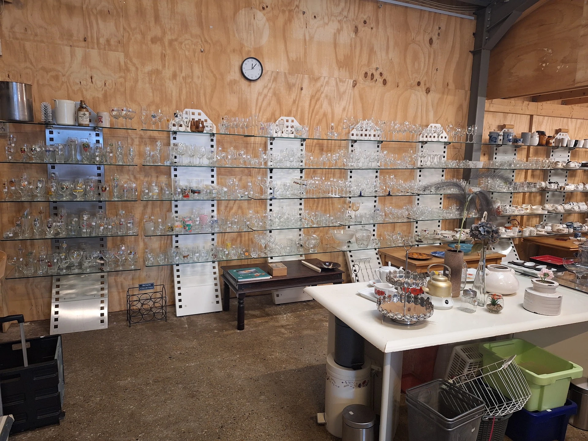 Binnenkant van kringloopwinkel met glazen vitrinekasten vol glaswerk en verzamelobjecten tegen houten wand
