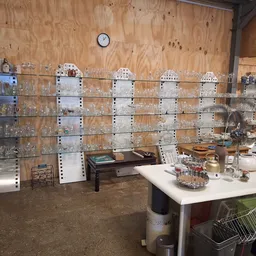 Binnenkant van kringloopwinkel met glazen vitrinekasten vol glaswerk en verzamelobjecten tegen houten wand