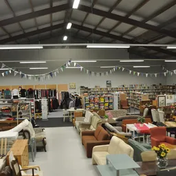 Overzicht van kringloopwinkel met meubels, kleding, boeken en huishoudartikelen verspreid over de vloer en in stellingen