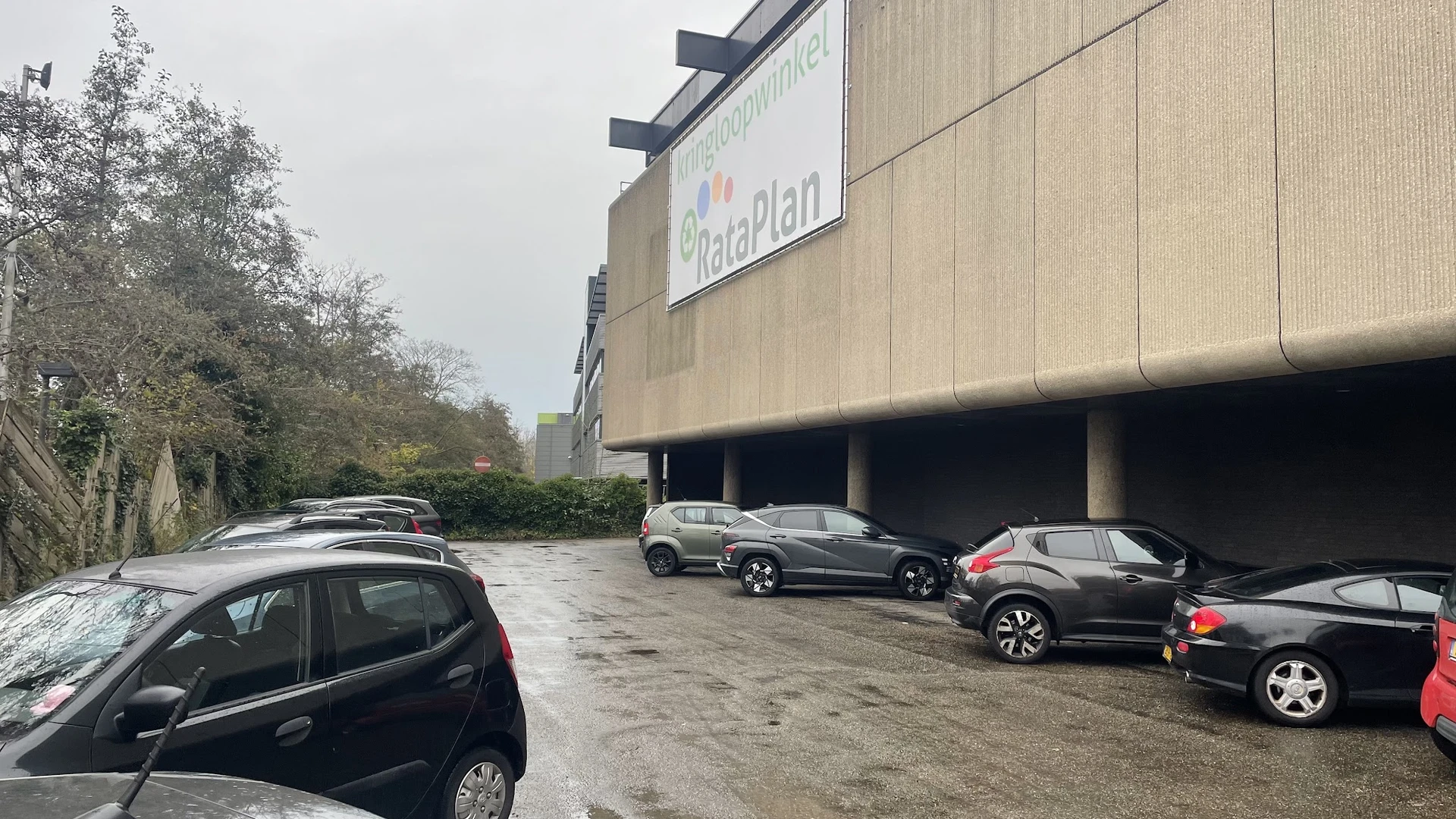 Parkeerplaats met geparkeerde auto's voor een betonnen winkelgebouw met Rataplan-signage