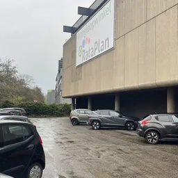 Parkeerplaats met geparkeerde auto's voor een betonnen winkelgebouw met Rataplan-signage