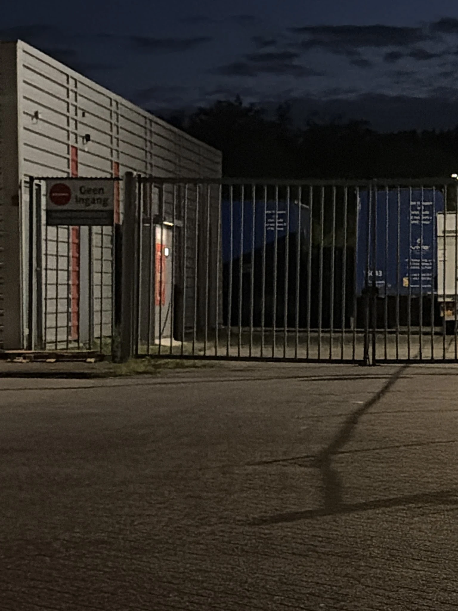 Gesloten poort en hek van kringloopwinkel 's avonds, voorkant gebouw met ramen zichtbaar