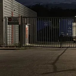 Gesloten poort en hek van kringloopwinkel 's avonds, voorkant gebouw met ramen zichtbaar