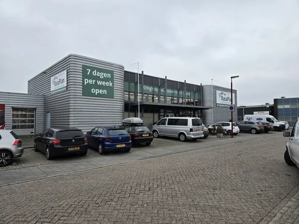 Grijze gevel van kringloopwinkel met witte letters 'Kringloop' en 'Kringloop 7 dagen per week open' op donkere ochtend, parke