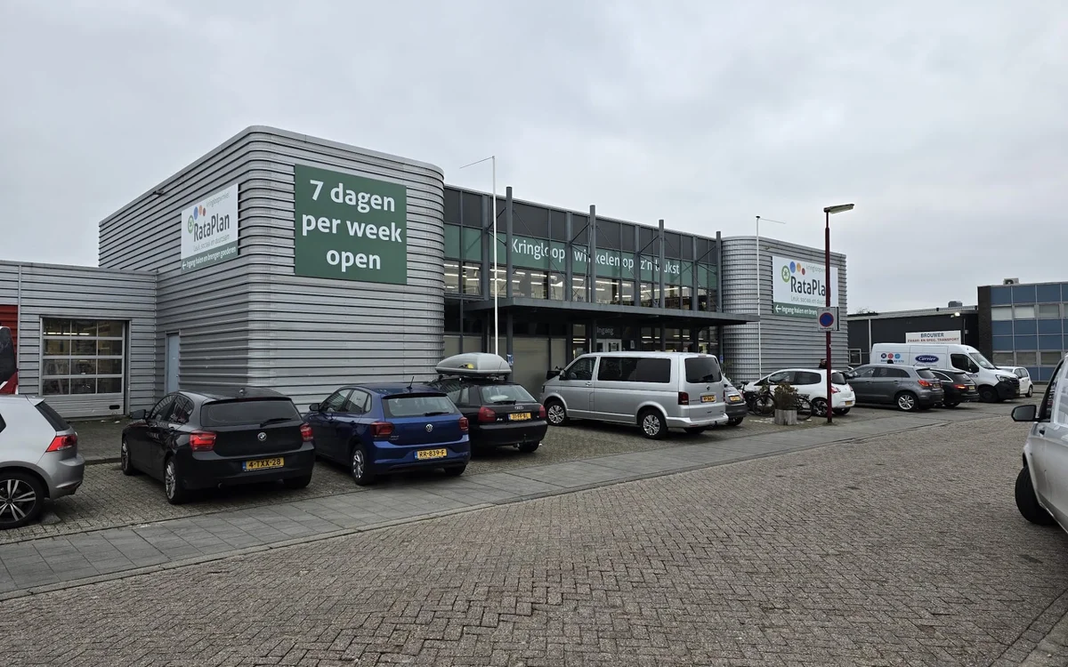 Grijze gevel van kringloopwinkel met witte letters 'Kringloop' en 'Kringloop 7 dagen per week open' op donkere ochtend, parke