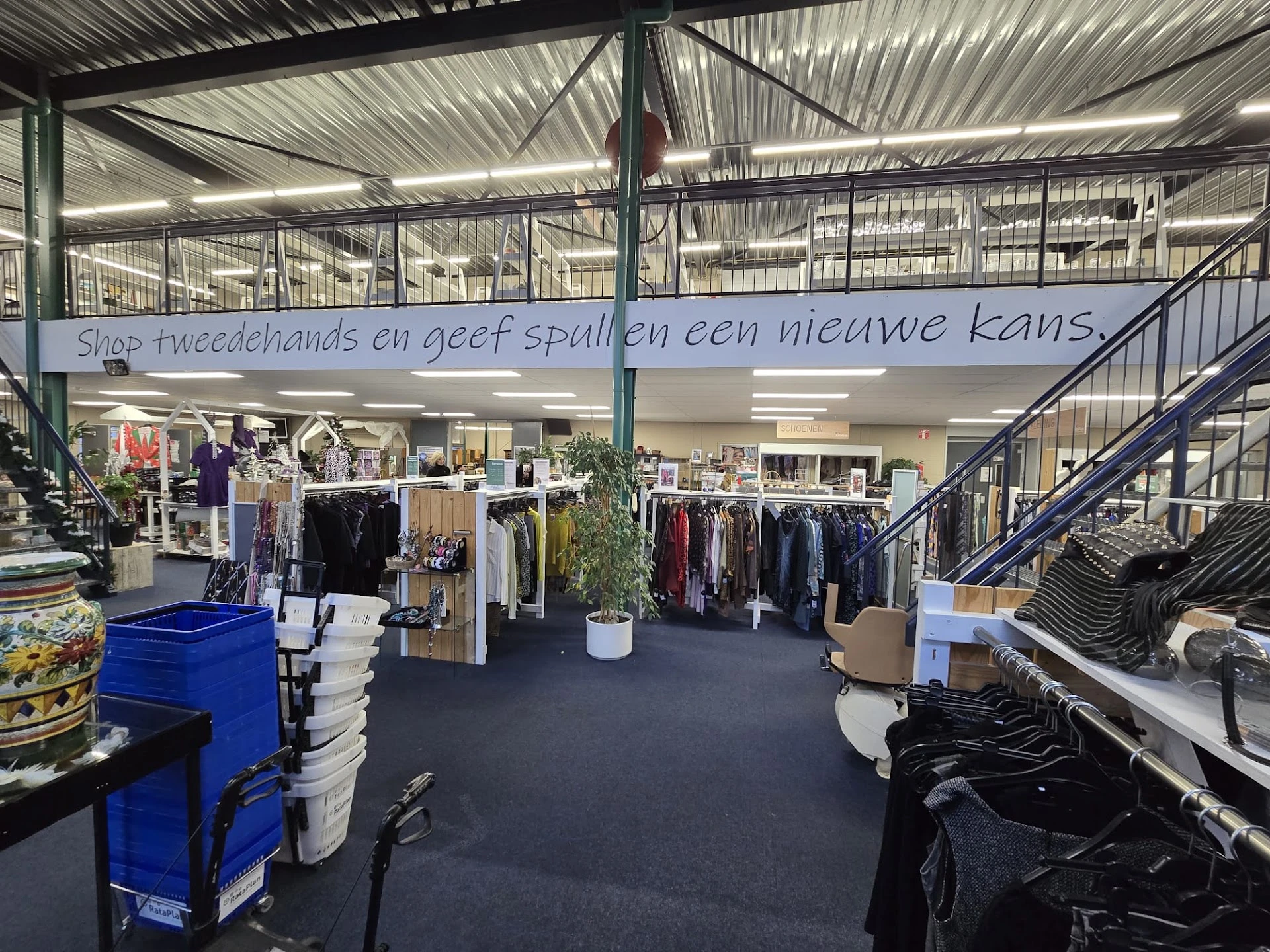 Winkelhal met kledingrekken, stellingen en diverse tweedehands artikelen op donkere vloer