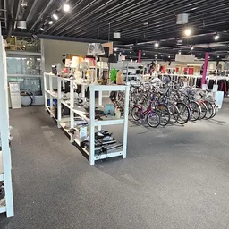 Ruim winkelinterieur met witte stellingen, fietsrek met fietsen, kleding aan rekken en spotverlichting aan plafond
