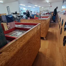 Winkelvloer met houten displaykasten en rekken vol tweedehands artikelen, personeel in het achtergrond