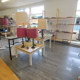 Winkelvloer met houten tafels, rode stoelen, houten stellingen en diverse winkelspreiding