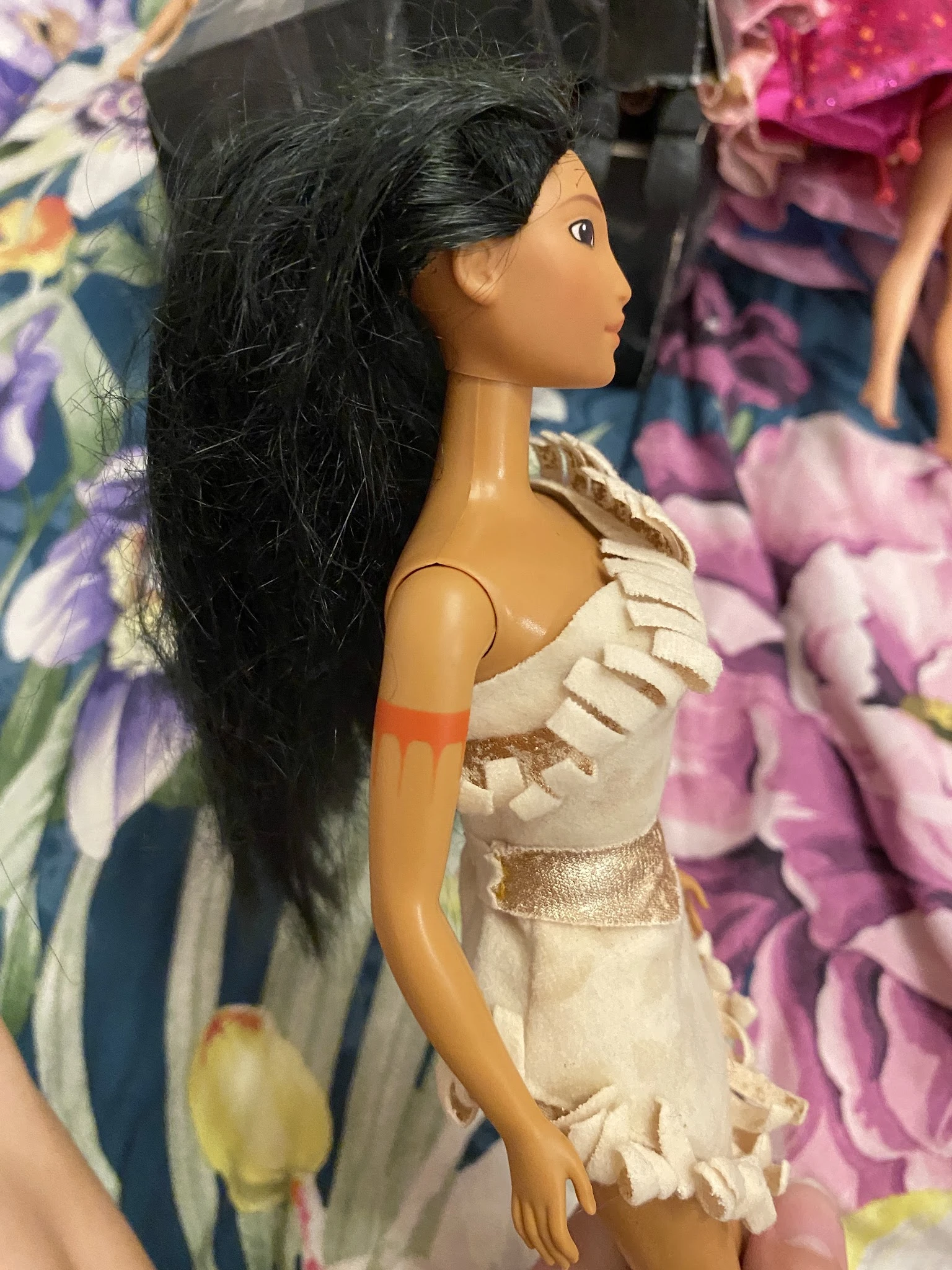 Close-up van een barbiepop met lange zwart haar, gekleed in een beige jurk met gouden details