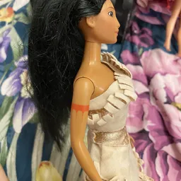 Close-up van een barbiepop met lange zwart haar, gekleed in een beige jurk met gouden details