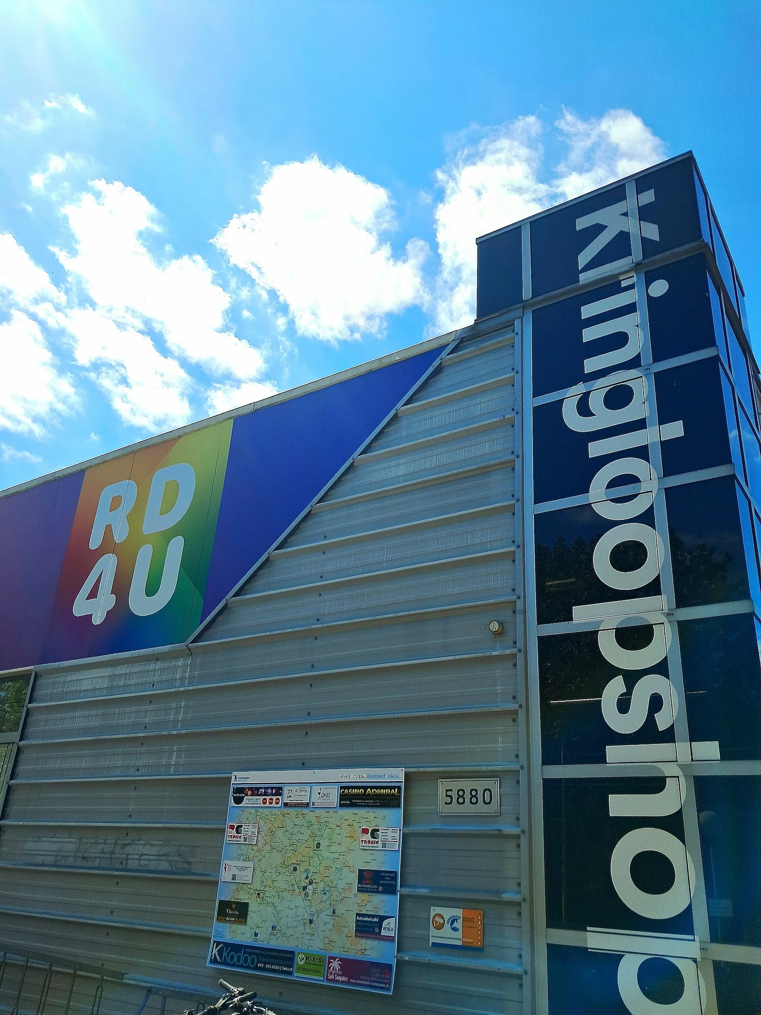 Voorkant van kringloopwinkel met blauwe luifel en winkelnaam 'RD4U' en 'IsodoNaum' op de zijkant
