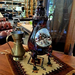 Close-up van een donkerrode glazen fles met decoratief winterlandschapbeeld en een gouden koperen kruik op houten tafel
