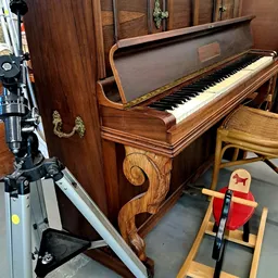 Houten vleugelpiano in bruine kleur met zichtbaar toetsenbord en ornamentale details aan de zijkant