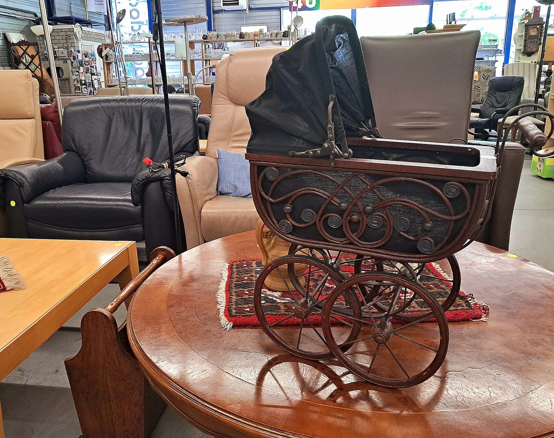 Antieke kinderwagen met houten decoratief frame en rode wielen, op een houten tafel in de winkel